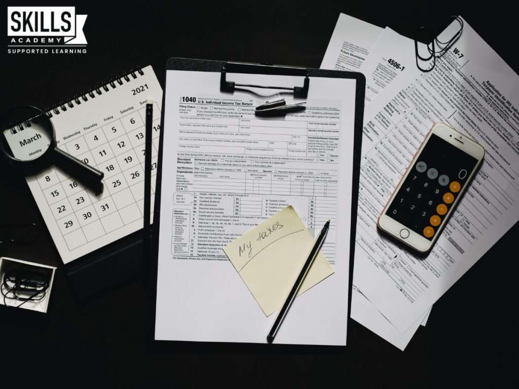 税务表格，计算器和日历放在桌子上。学习您需要的财务技能与我们的簿记课程。