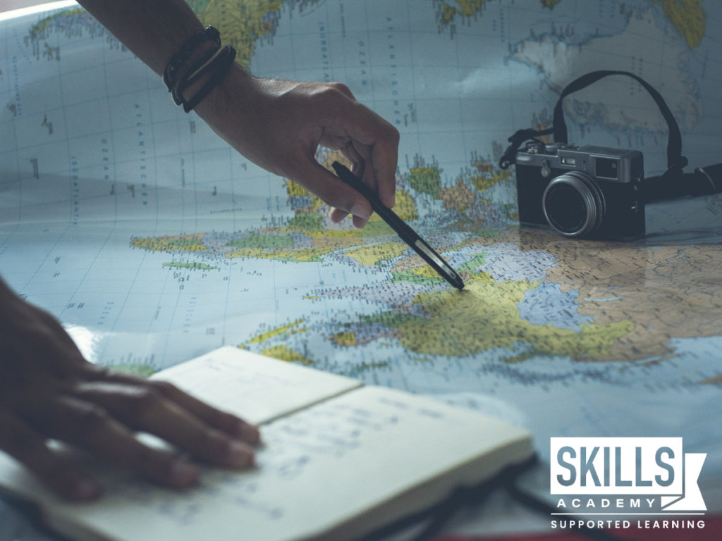 一个人站在地图上，旁边放着笔和相机。我们的旅游课程将教给你在旅游业中蓬勃发展所需的宝贵技能。