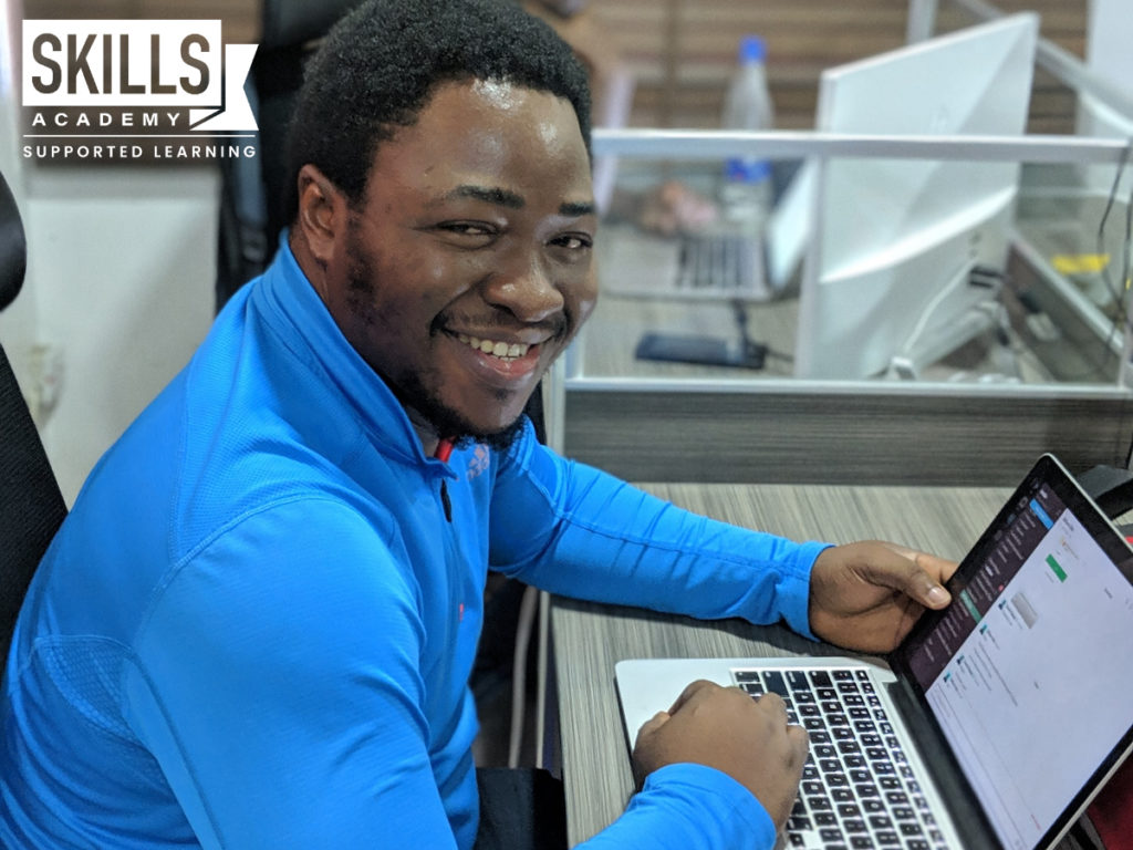 一名穿着蓝色衬衫的男子在笔记本电脑前工作，使用他在我们的小企业管理课程中学到的技能。