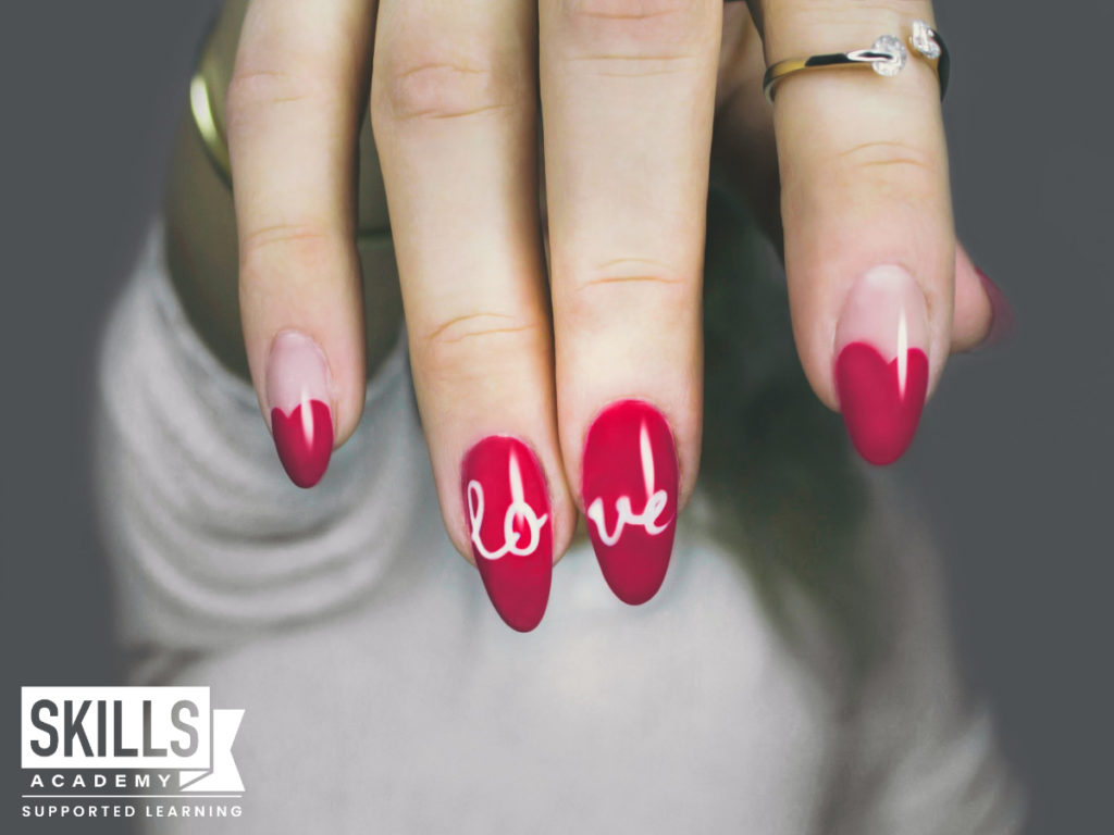 女人的手涂着红色的指甲油，食指和中指上写着“爱”两个字。与我们一起学习精益指甲应用技能。