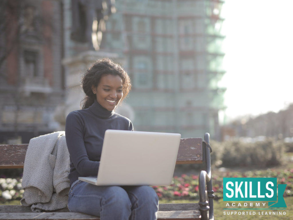 一个年轻的学生坐在公园长凳上用笔记本电脑学习远程教育课程。