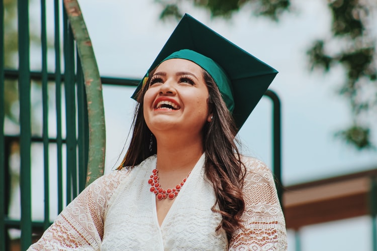 一个年轻的女孩,一段裙子,橙色项链和她的绿色毕业上限是高兴地笑着仰望天空,因为她为求职者接受了我们的建议
