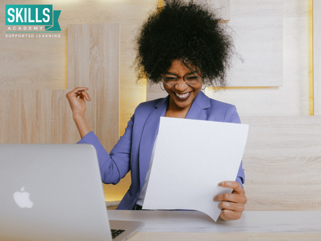女人穿着紫色的运动夹克，手里拿着文书，面带微笑。职场技能会提高你的工作效率和自信。
