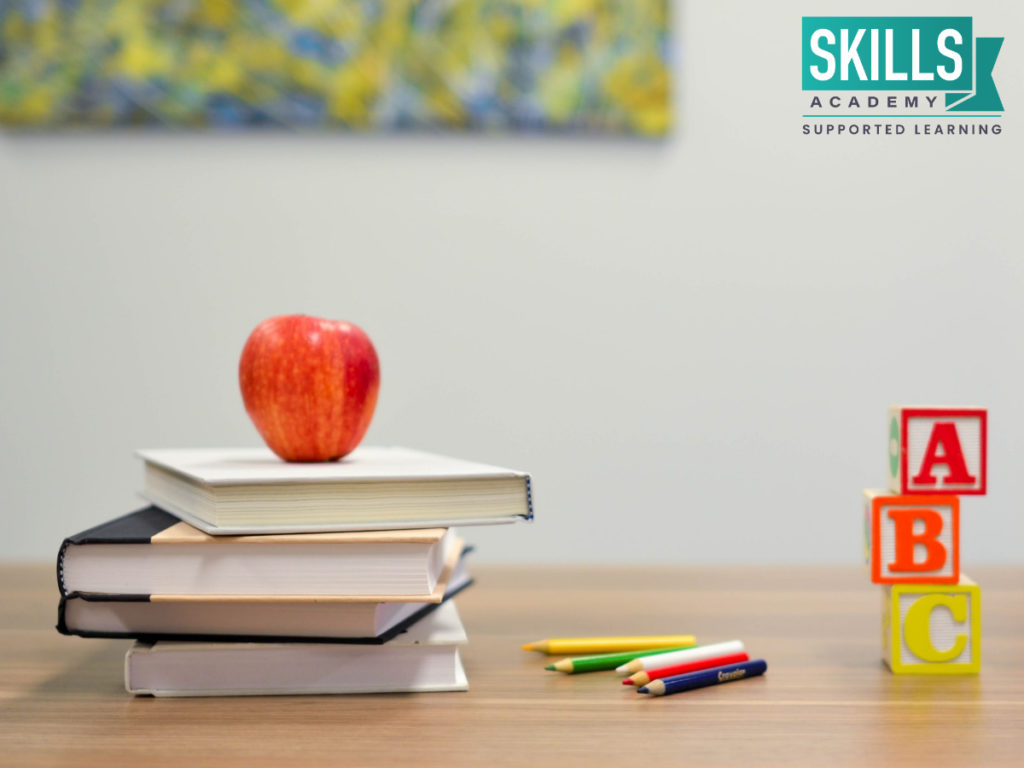 四本书堆放在一个苹果和彩色铅笔旁边。通过我们的教育和儿童护理课程，使自己具备所需的技能和知识。