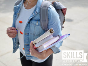 一个穿着牛仔夹克和白t恤的大学生，左臂上挎着书，背上背着背包