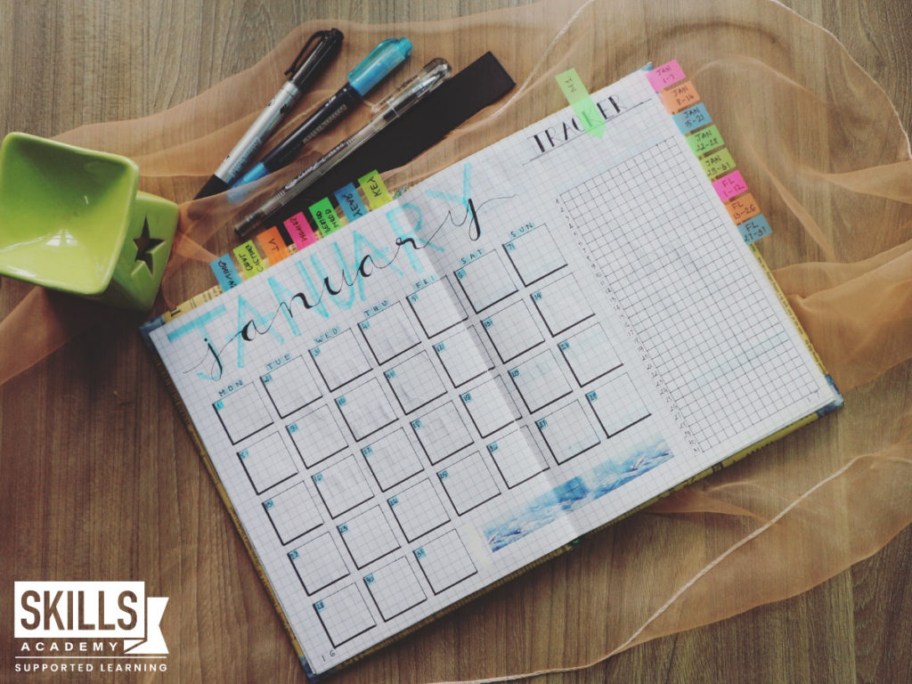 桌子上放着一张月计划表和几支彩色笔。这些工具可以帮助你学习如何保持你的学习目标