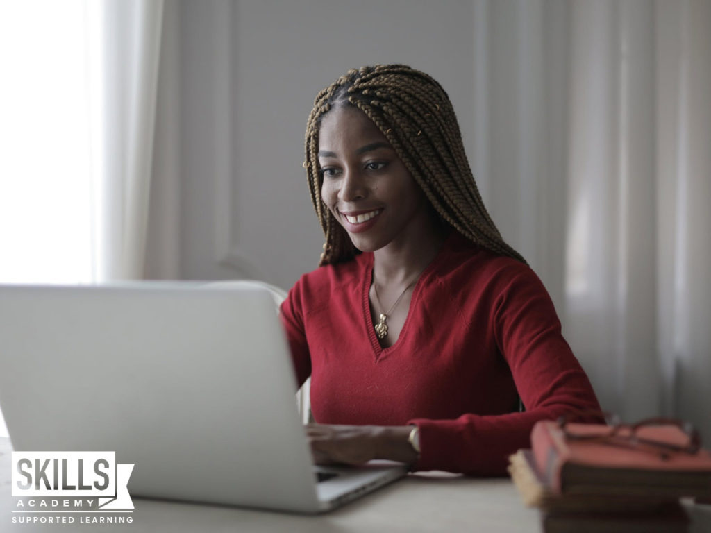 一个年轻的学生穿着一件红色上衣,坐在电脑前,看着信息,帮助她决定她应该学习或工作在大学入学考试。
