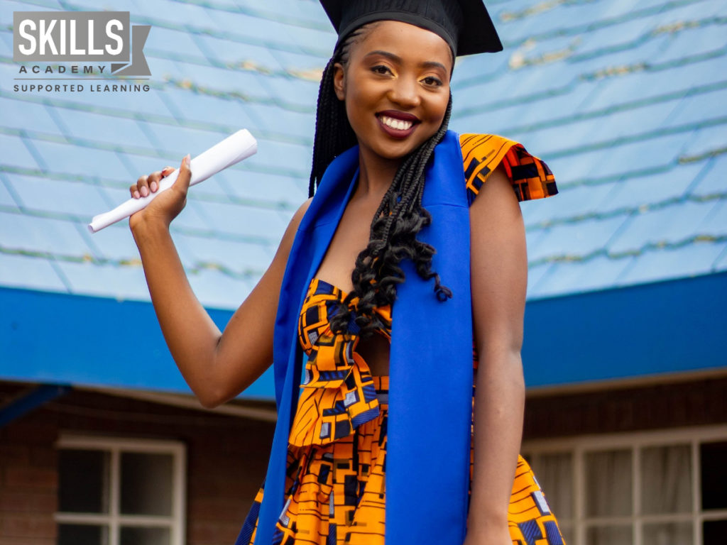 毕业生面带微笑，手里拿着毕业证，站在一栋大楼前。如果你知道如何为新年设定目标，你也可以成功。