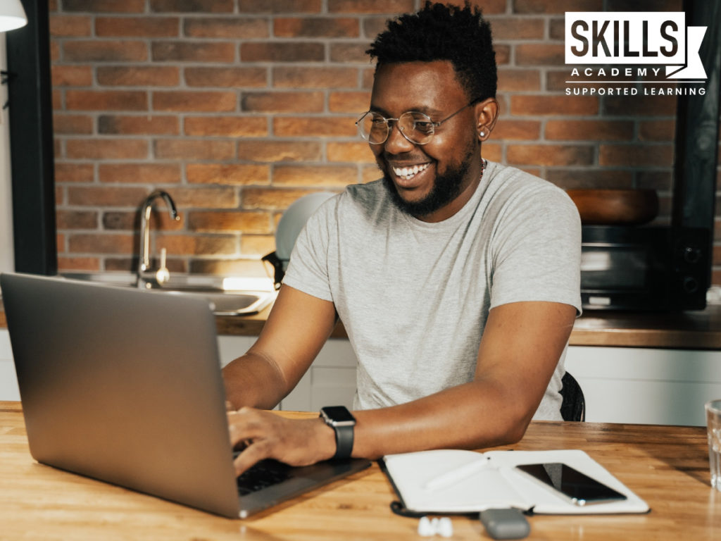 一个男人在电脑上工作，微笑着，因为他要搜索如何为新年设定目标，这样他就可以计划他的新年决心。
