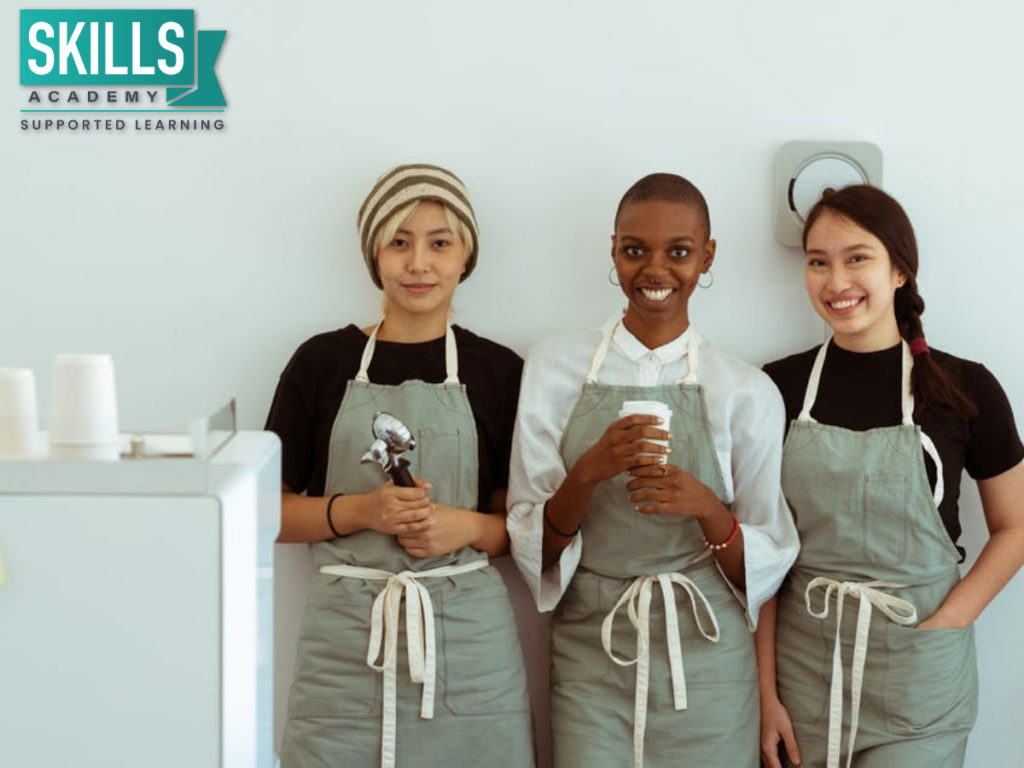 三个女人在围裙在咖啡店工作。谁能成为企业家?与我们的课程你可以得到所需的所有技能开始你的小生意。