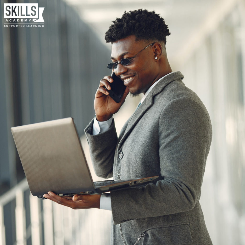 男人穿西装和太阳镜的微笑虽然看着笔记本电脑和手机聊天。学习技能需要与我们的课程,这将提高你的领导能力。