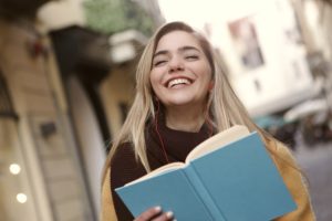 微笑的学生拿着一本书。为乐趣而阅读是期末考试后要做的事情之一