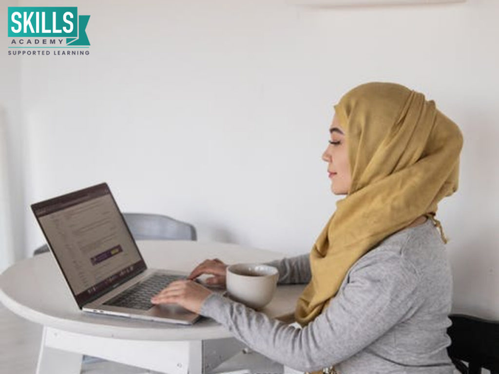 一个年轻的穆斯林女孩戴着面纱,坐在她面前的桌子上电脑,了解如何通过补充考试。