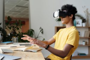 一个学生戴着虚拟现实眼镜坐在课桌前上课。这是教育中的技术。