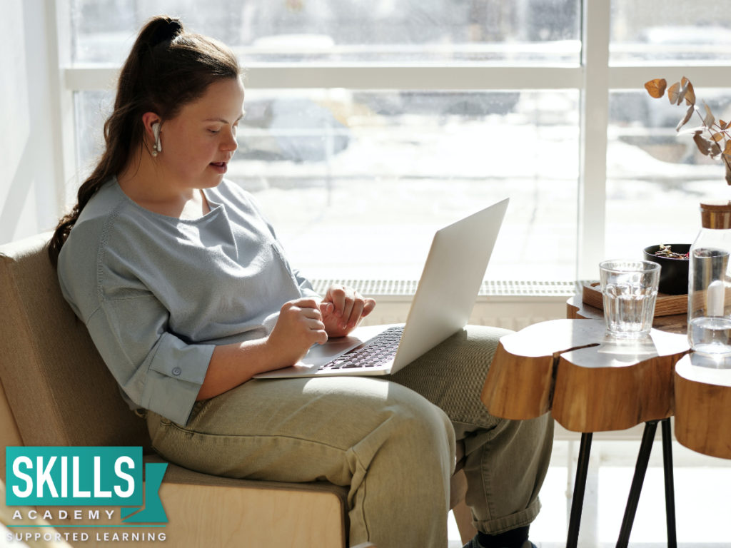 一个学生拿着一台银色笔记本电脑坐在咖啡馆的窗前，做着她的工作。以下是关于ICB考试注册2021年的更多信息