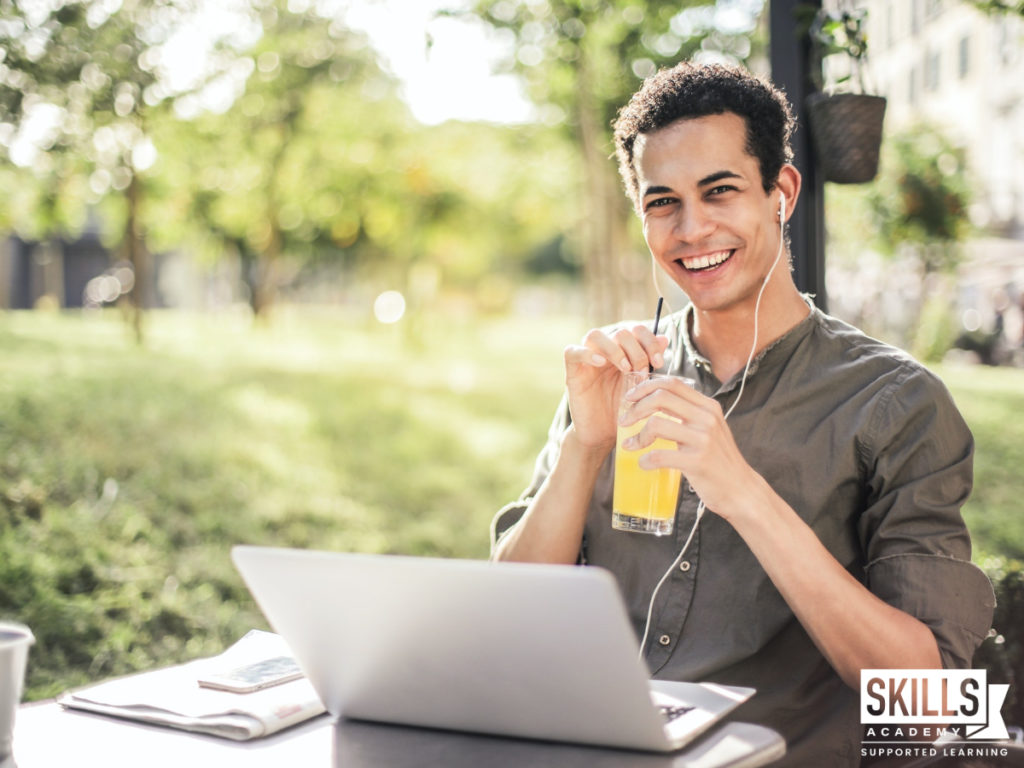 男人微笑着拿着一杯果汁，坐在外面的长凳上，面前放着一台笔记本电脑。随时加入技beplay世界杯安卓APP下载能学院，你可以在任何地方学习。