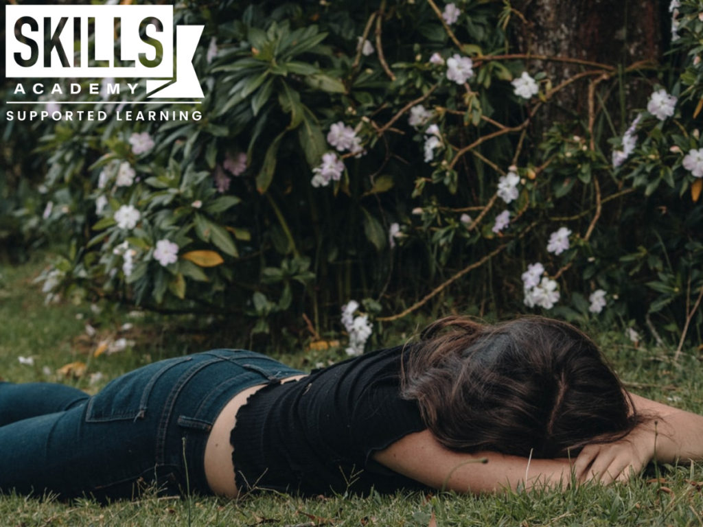 Woman laying on grass, her face tucked in between her arms. This is how you can handle study burnout