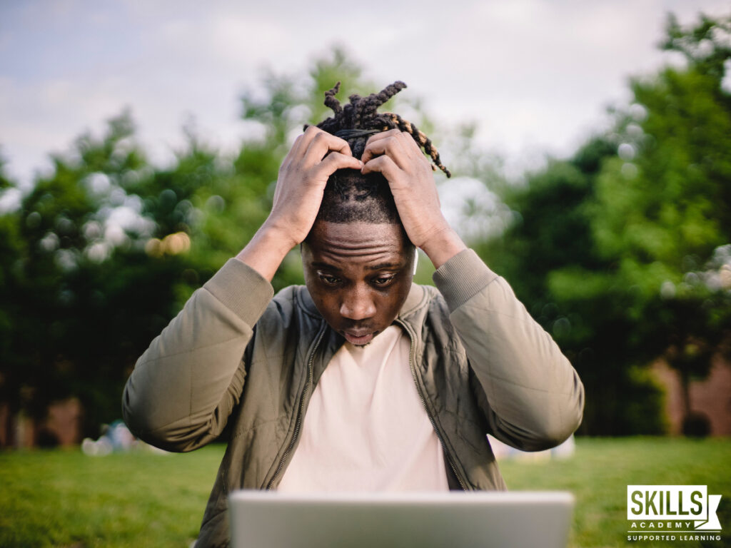 学生用他的笔记本电脑坐在外面草坪上用手在他的头上。什么是你的选择,如果你考试失败的ICB吗?找到这里。