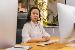 一个年轻女人戴着耳机和坐在电脑前学习所有技能后每个办公室管理员的需求。今天学习我们学院的课程!