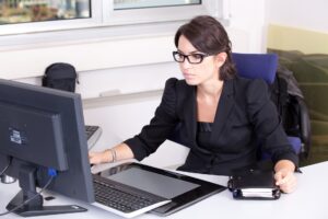 一个年轻的办公室管理员坐在她的办公桌回答电子邮件。检查办公室管理准入要求。